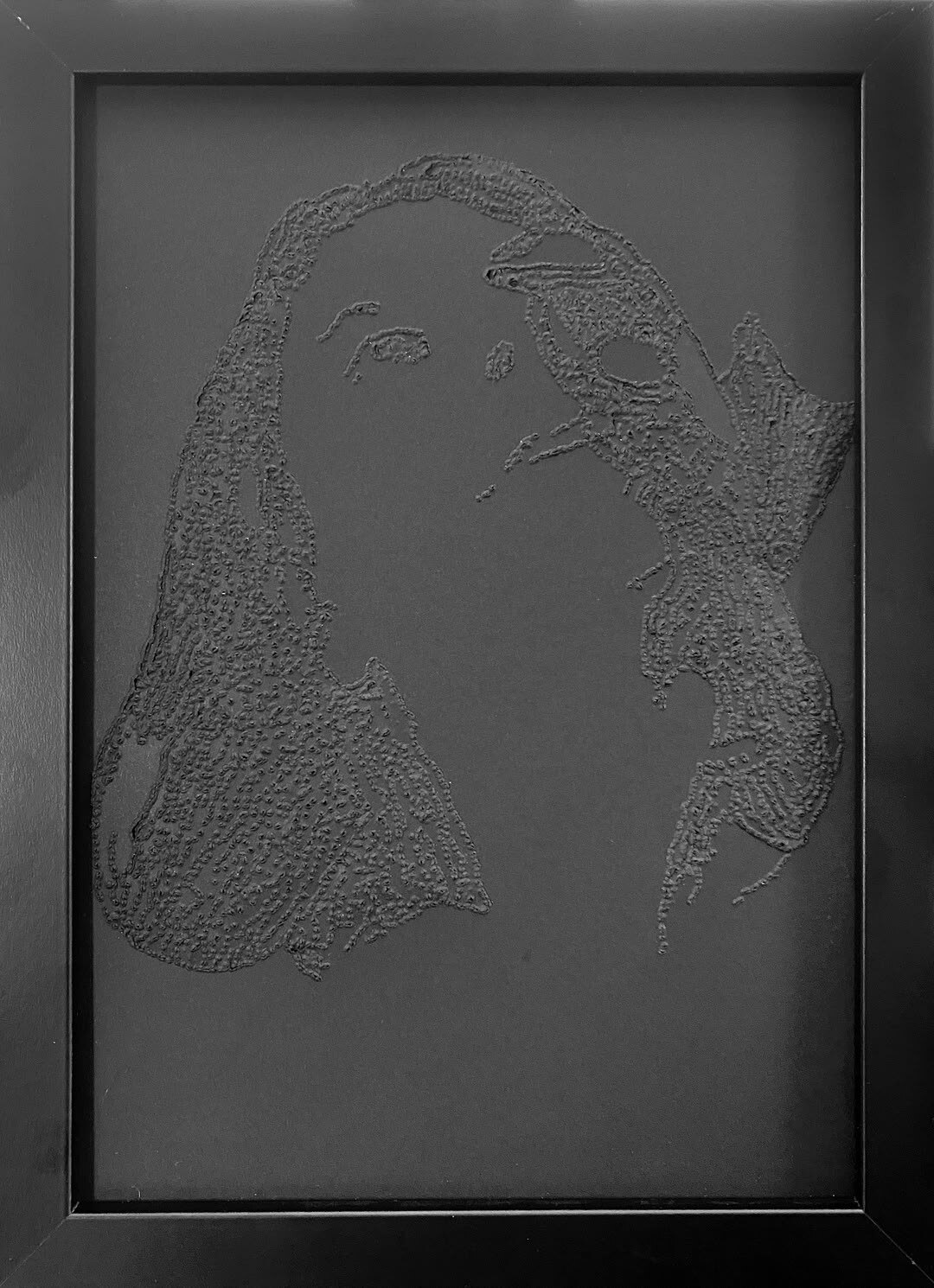Pionowy relief punktowy na czarnym kartonie, w czarnej ramie. Twarz jest mocno odchylona ku górze. Dłoń oparta na czole przechodzi nad jednym okiem, a gęste włosy opadają szerokim pasmem po lewej stronie kompozycji.