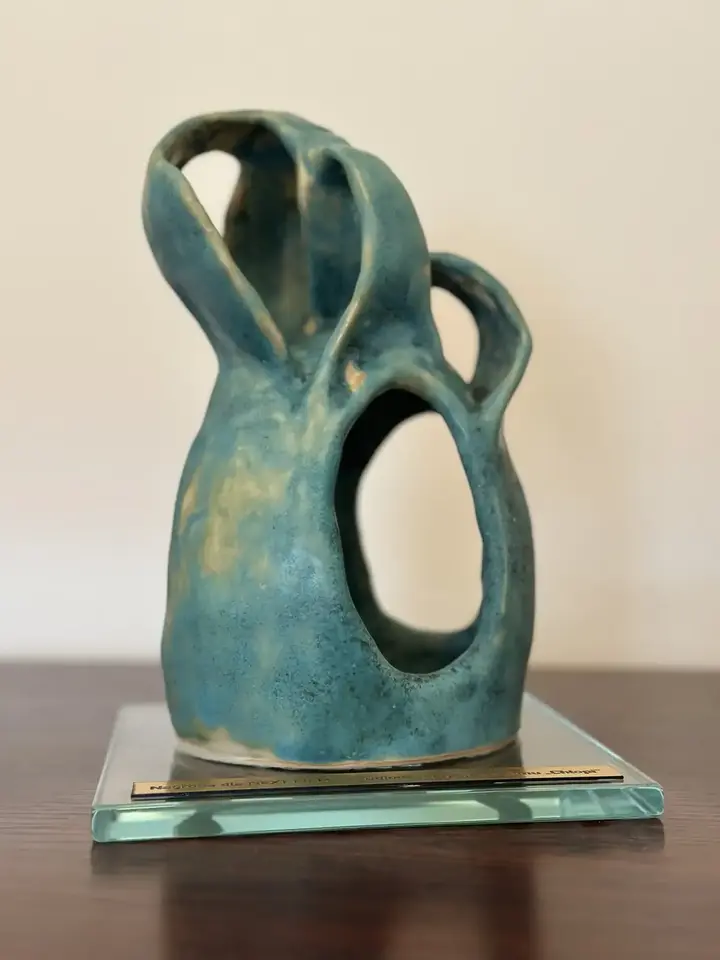 Turkusowo-zielona statuetka ceramiczna z łukowymi pasmami i nieregularnymi prześwitami.