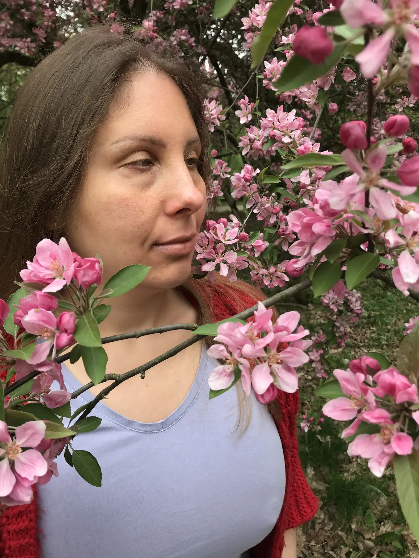 Magdalena Rutkowska pośród gęstych gałęzi obsypanych różowymi kwiatami. Jej twarz otaczają kwiaty i zielone liście; artystka patrzy w bok.